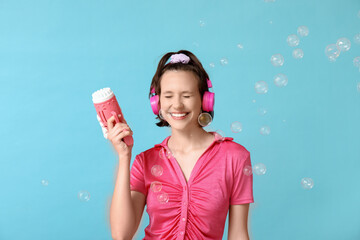 Happy teenage girl in headphones with soap bubble gun on blue background