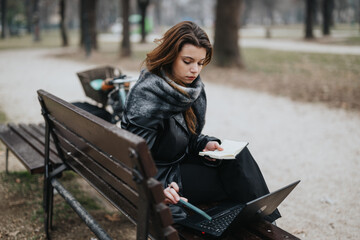 Stylish young woman confidently working outdoors on a laptop while sitting on a park bench.