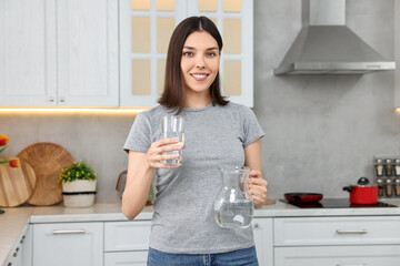 Woman with jug and glass of water in kitchen