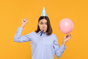 Young woman in party hat with balloon and blower on yellow background