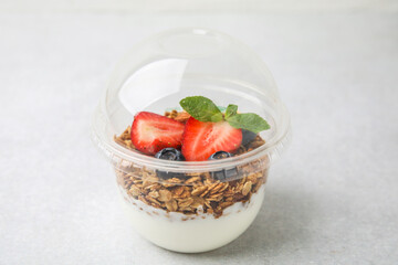 Tasty granola with berries and yogurt in plastic cup on light table, closeup