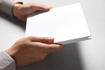 Man holding blank book at light grey table, closeup. Mockup for design