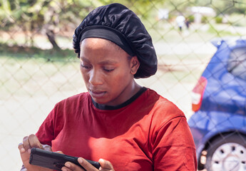 young african woman shopkeeper using a smartphone in front of the shop in the poor township,...