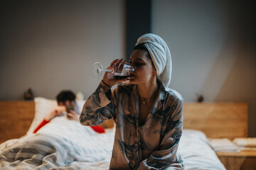 Intimate home setting with a couple unwinding in bedroom, woman sipping wine and man on phone.