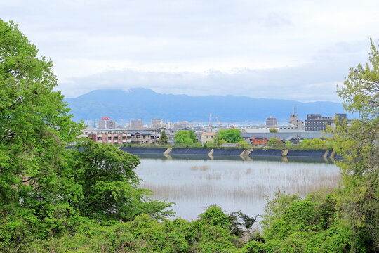 雲がかかった比叡山と麓にわずかに見える琵琶湖、ため池と街の建物