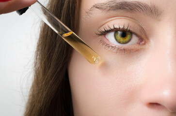 Happy young woman applying serum on her face with her eyes open.