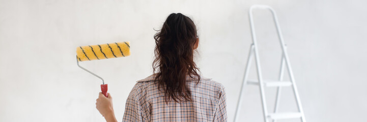 Back View of Painter Woman With Paint Roller on Gray Wall Background