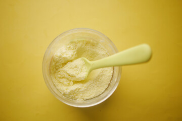 top view of baby milk powder and spoon on yellow background.