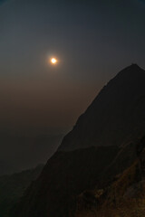 A mountain with a large moon in the sky