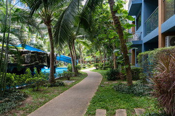 A concrete path running between the building and the pool with a slide among tropical vegetation at the resort.