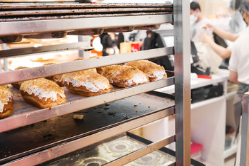 Freshly baked bread on trays at pastry store with workers on the background