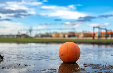 Selective focus on mud in front of a basketball sitting in a mudpuddle of water at a school playground.