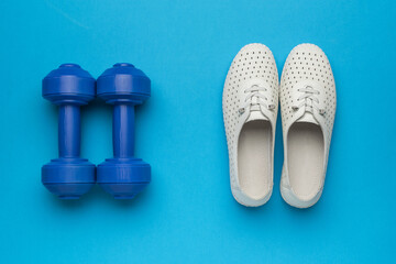 White athletic shoes and blue dumbbells on a blue background.