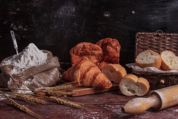 Freshly bread baguettes and muffins on a wooden table in a dark studio