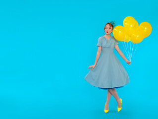 Pin-up girl in dress and heels with yellow balloon on blue background with copy space
