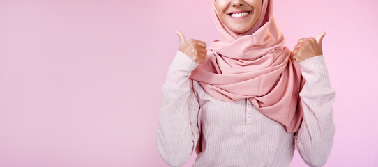 Like gesture. Perfect choice. Unrecognizable satisfied smiling happy woman in hijab showing approval thumbs up isolated on pink empty space background. - 792295806
