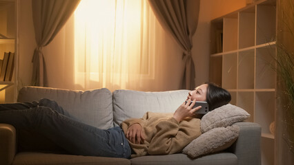 Phone talk. Home leisure. Weekend communication. Relaxed woman speaking lying on cozy couch in...