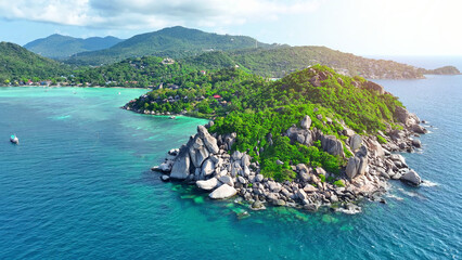 Mesmerizing coastal vista, Rocky shore meets lush forests against a backdrop of azure seas, a breathtaking blend of nature's hues from above. Aerial view from drone. Koh Tao, Thailand. 
