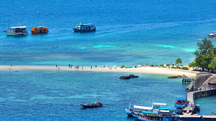 Tourists flock to a sandbar, encircled by boats, in pristine azure waters, a vibrant scene of...