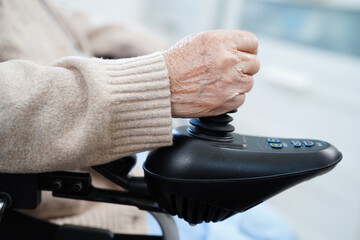 Asian elderly disability woman patient use joystick electric wheelchair in hospital.