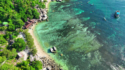 Emerald forests fringe the rugged coastline, adorned with distinctive rock formations, while pristine turquoise waters beckon with their serene beauty. Aerial view. Koh Tao, Southern Thailand. 
