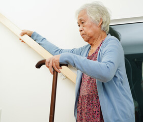 Asian senior woman use walking stick with caregiver help support walking down the stairs prevent...