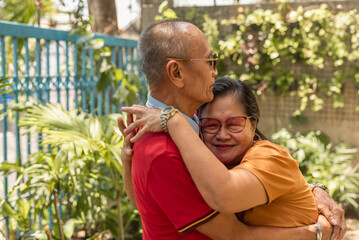 A old asian woman hugs her long-time husband of 40 years. An affectionate and loving couple in their late 60s to early 70s. Outdoor scene.