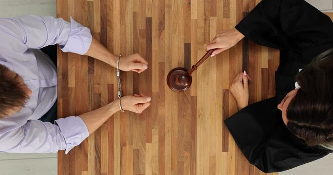 Man in handcuffs and a judge with gavel in courtroom top view