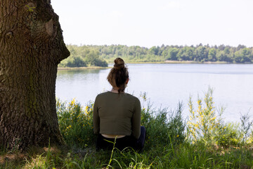 This evocative image depicts a woman from behind, sitting in stillness by a tranquil lake. Flanked...