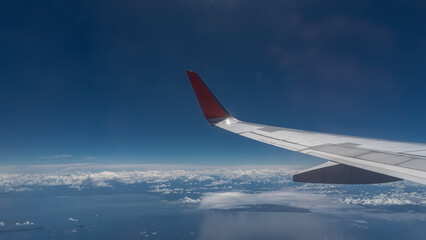Islands in the blue ocean are visible from the plane. Clouds are reflected in the water. Azure sky. The wing of the aircraft is in the foreground. Malaysia.