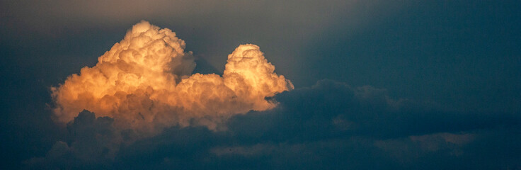 Cloud in the sky at sunset. The cloud is illuminated by the rays of the sun on the dark sky in the...