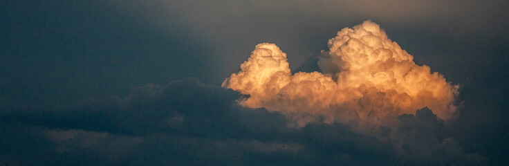 Cloud in the sky at sunset. The cloud is illuminated by the rays of the sun on the dark sky in the evening. A light cloud among thunderclouds in the sky.