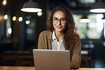 Photo of beautiful happy woman looking at camera while sitting at office. using laptop