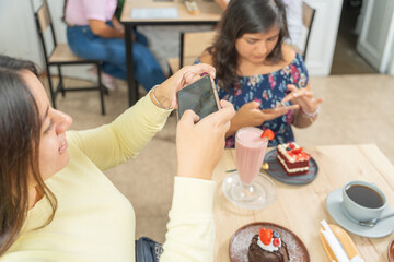 Girlfriends eating dessert in a cafeteria taking pictures of their food