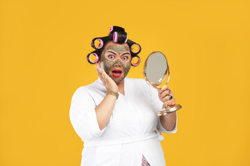 Portrait of fat and happy housewife wearing a natural mask looking in the mirror isolated on a...