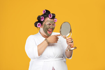 Portrait of fat and happy housewife wearing a natural mask looking in the mirror isolated on a...