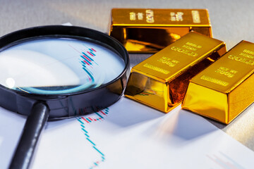 Magnifying glass with gold bars on  rising price graph.