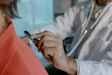 A doctor is examining a patient in a private examination room to check blood pressure and heart...