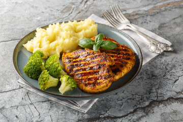 portion of grilled chicken breast with a side dish of mashed potatoes and broccoli close-up in a...