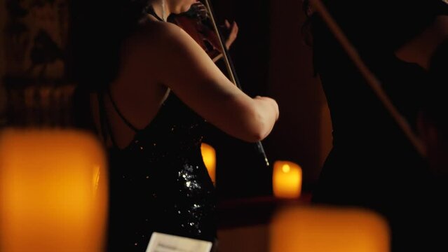 A woman in an evening dress on a stage with candles playing the violin. Focus on the hand and bow. Fine mastery of the instrument. Symphonic show by candlelight