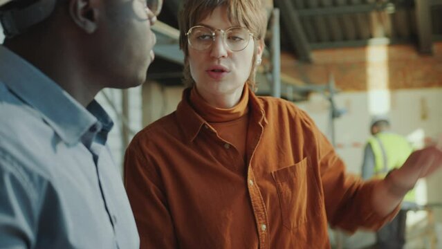 African American building contractor discussing architectural plan with Caucasian female client at construction site. Tilt-up shot, rack focus