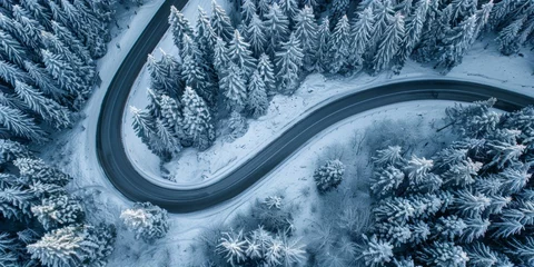 Stof per meter Aerial view of a curvy road snaking through a dense snowy forest in winter. © tashechka