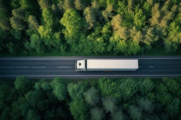 Fototapeten Large freight transporter semi truck driving on highway road moving through green forest with cargo semi trailer © The Big L