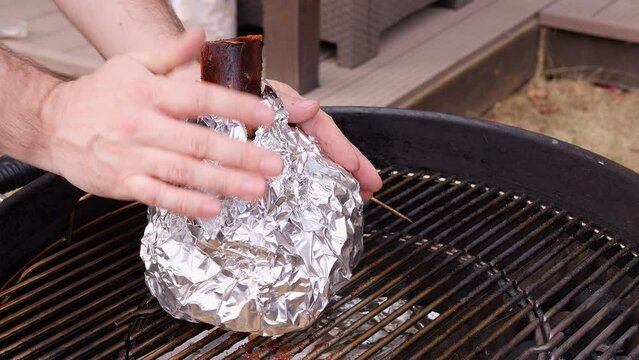 The chef places foil wrapped meat onto grill letting the heat work its magic The foil shields meat, preserving its tenderness and locking in favor. As the grill sizzles the foil ensures even cooking.