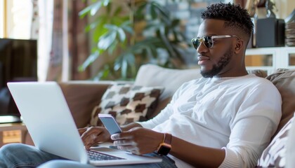Man using laptop and cell phone on couch with table nearby