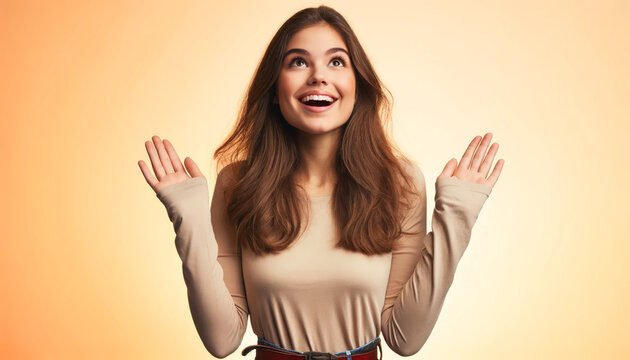A young woman with long brown hair, wide open eyes, and a big smile. She is expressing a joyful and surprised emotion, with both hands raised palms up at shoulder level as if presenting something. 