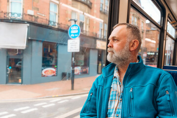 portrait of a bearded man in a blue jacket talking by phone on a bus or tram. Lifestyle concept