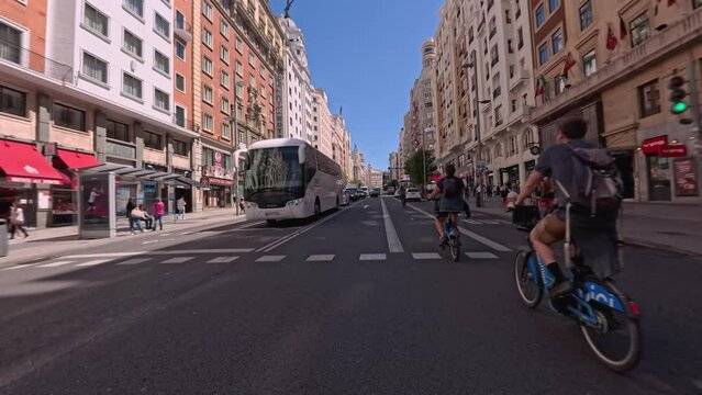 Personal perspective POV of a man riding his bike through Gran Vía street in Madrid on a sunny day from Spain Square to Callao Square with buses, taxis and cars circulating. POV Riding a city bike
