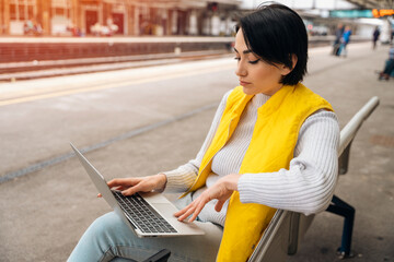 woman at railway station using computer, laptop. Working, studying, shopping, booking online....