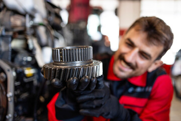 Experienced mechanic or serviceman holding gears parts inside workshop.